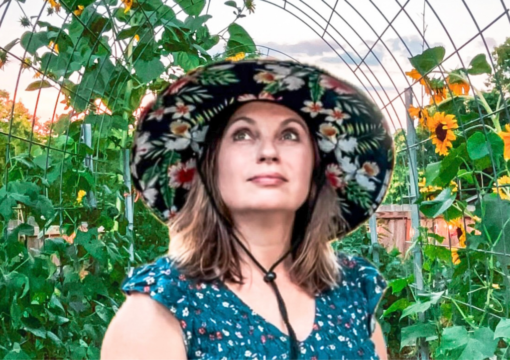 Woman gardener wearing a straw hat looking up at the sky in a lush home garden with flowers and vegetables