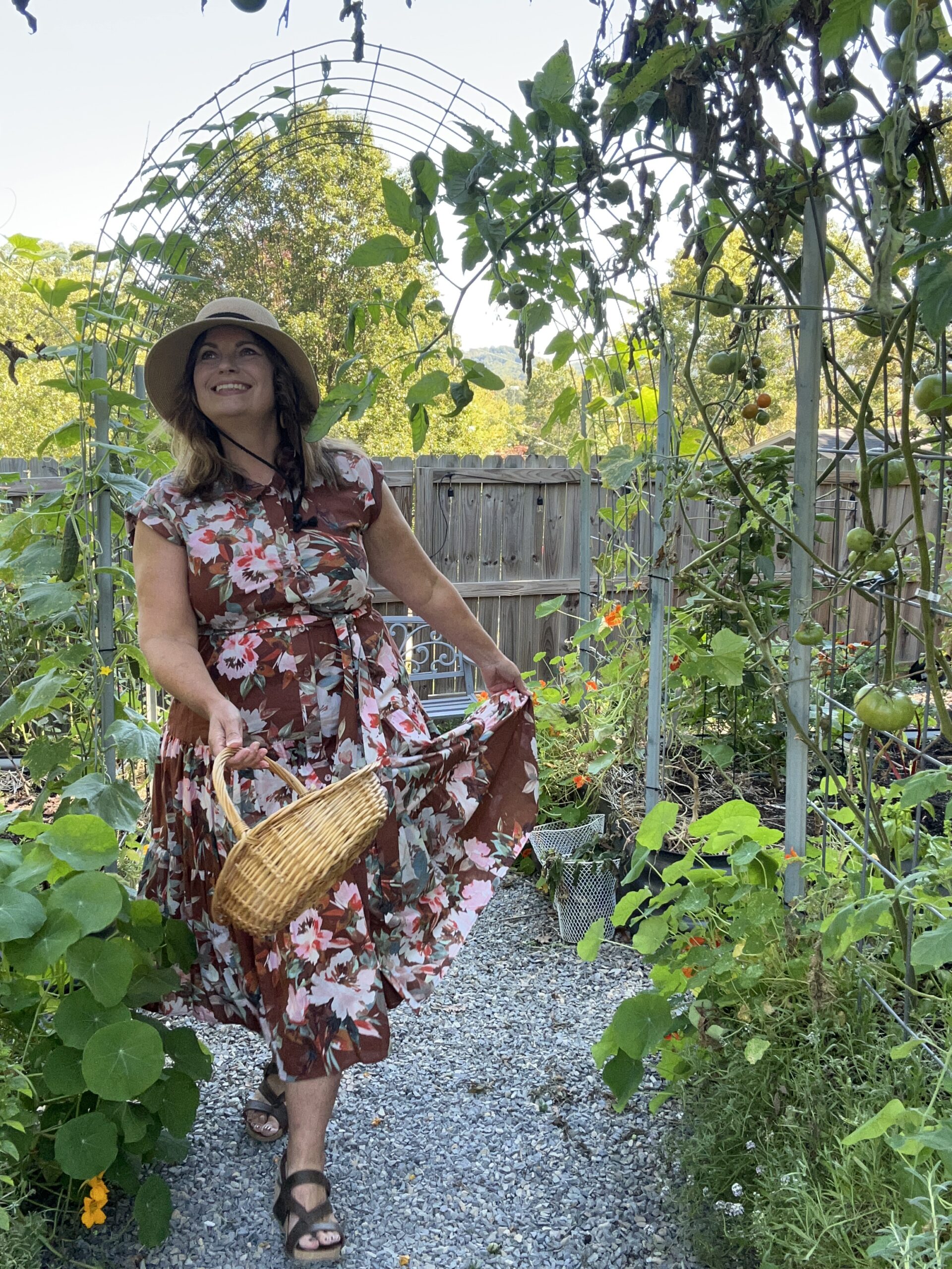 Woman in garden wearing a brown floral dress carrying a basket.
