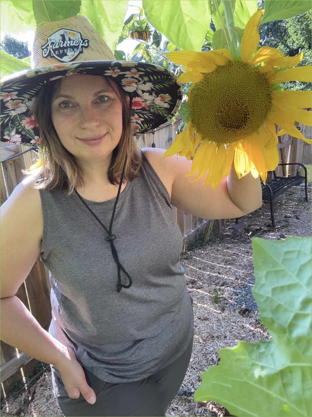 Woman in a straw hat holding a sunflower in a home garden.