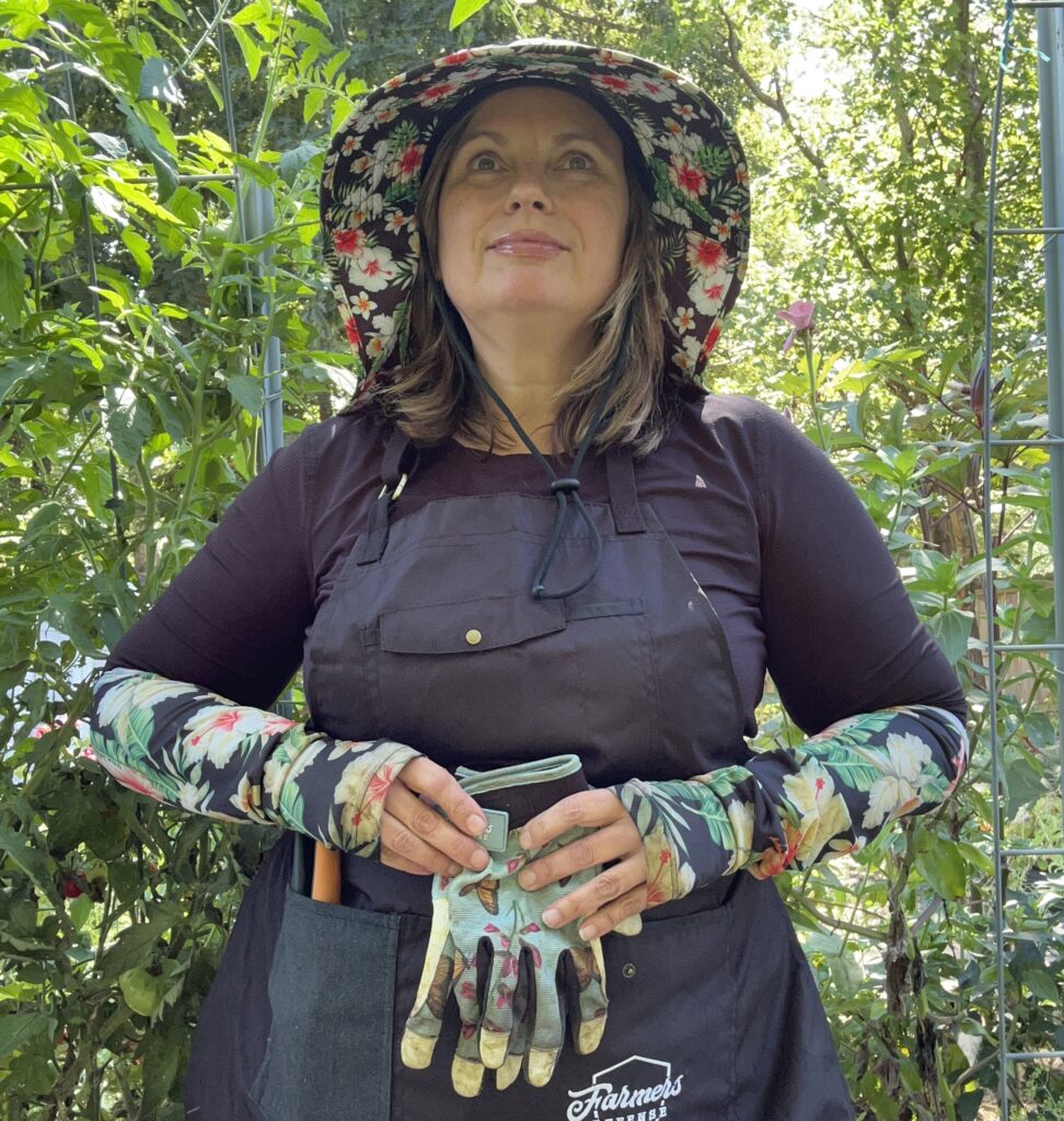 Woman standing in Garden with garden hat, sleeves, and gloves 