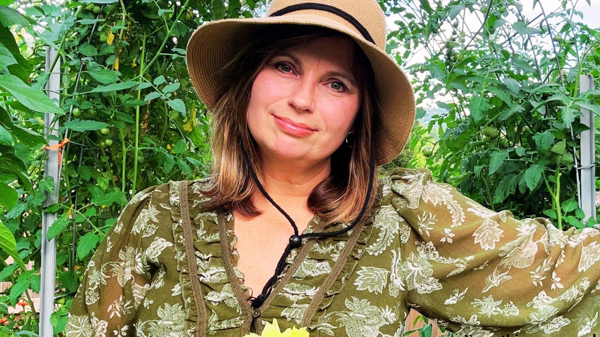 Gardener smiling in a lush garden wearing a green dress and sun hat