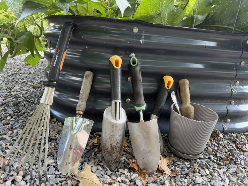 Garden tools leaning against a raised metal garden bed in the Michelle’s Garden Grows garden.